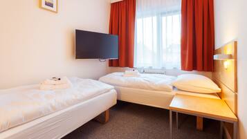 Habitación de hotel con dos camas individuales, un televisor de pantalla plana montado en la pared, una mesita de noche de madera y una ventana con cortinas rojas.