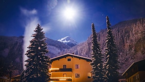 A mountain lodge with a snow-covered peak in the background, surrounded by evergreen trees. - Residence AlpenHeart (Bad Gastein)