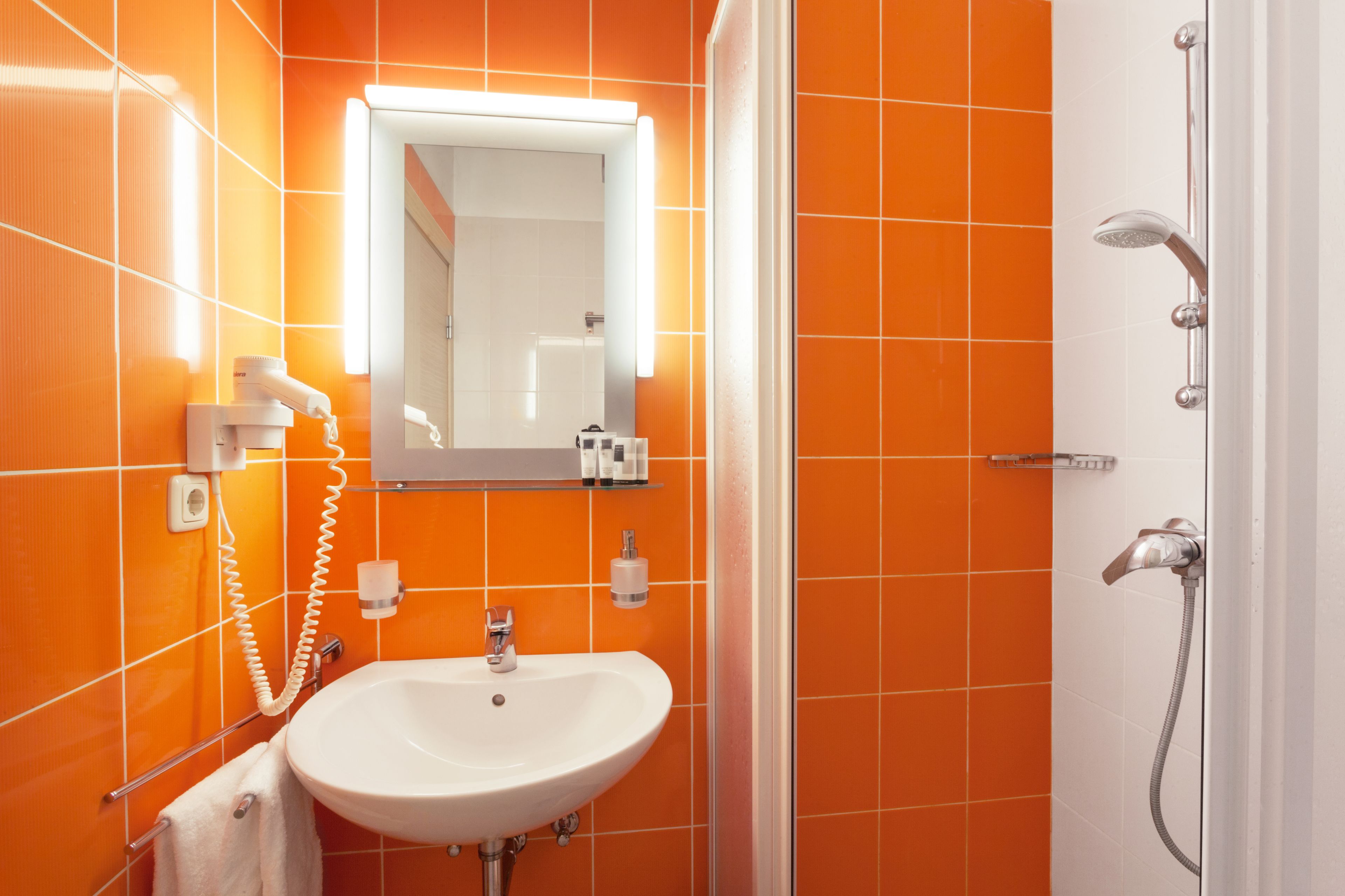 Un baño con baldosas anaranjadas, un lavamanos blanco, un espejo y una ducha.