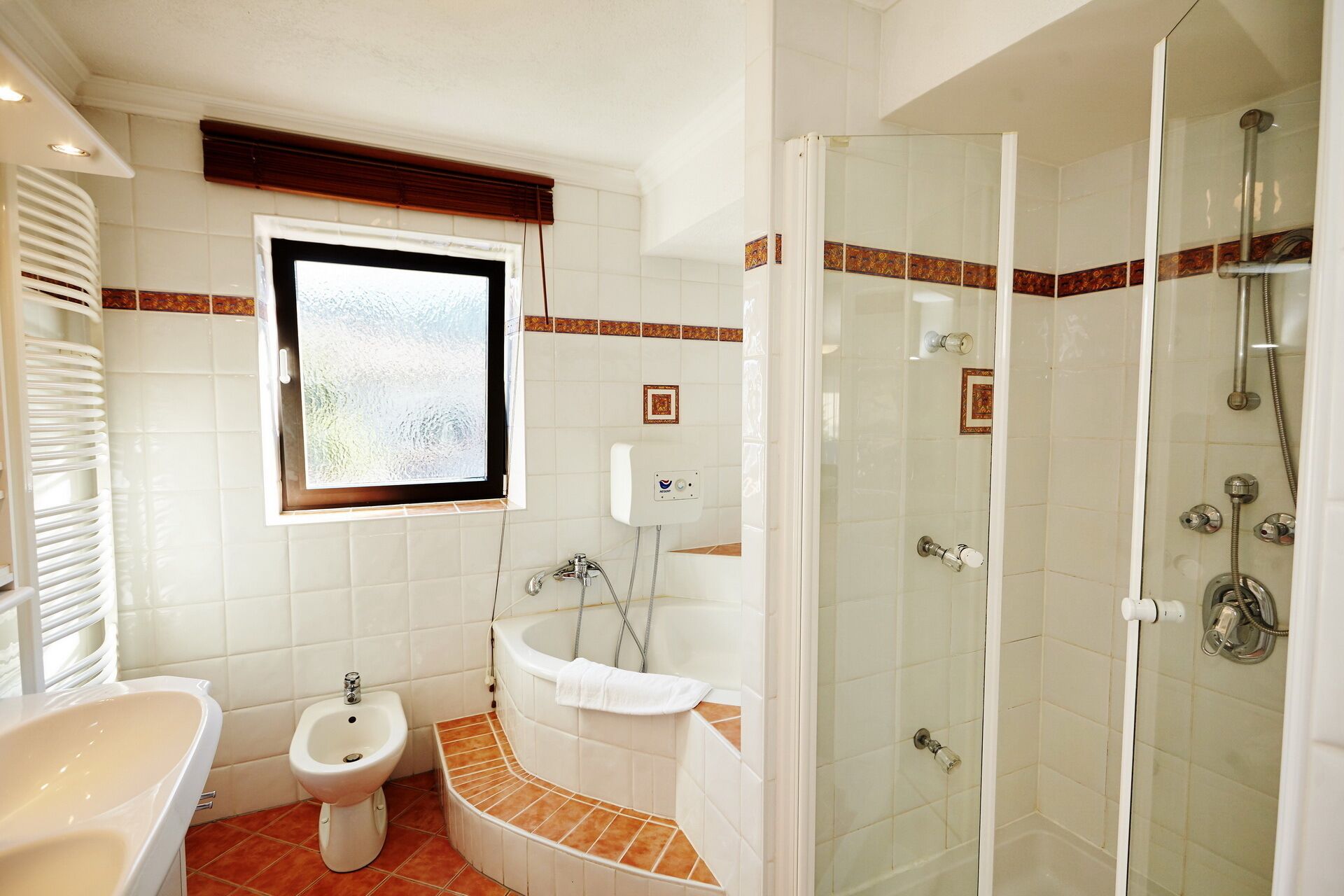 A bathroom with a bidet, a bathtub, and a glass-enclosed shower.