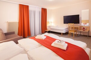 Habitación de hotel con cama, escritorio, silla, televisión y ventana con cortinas.