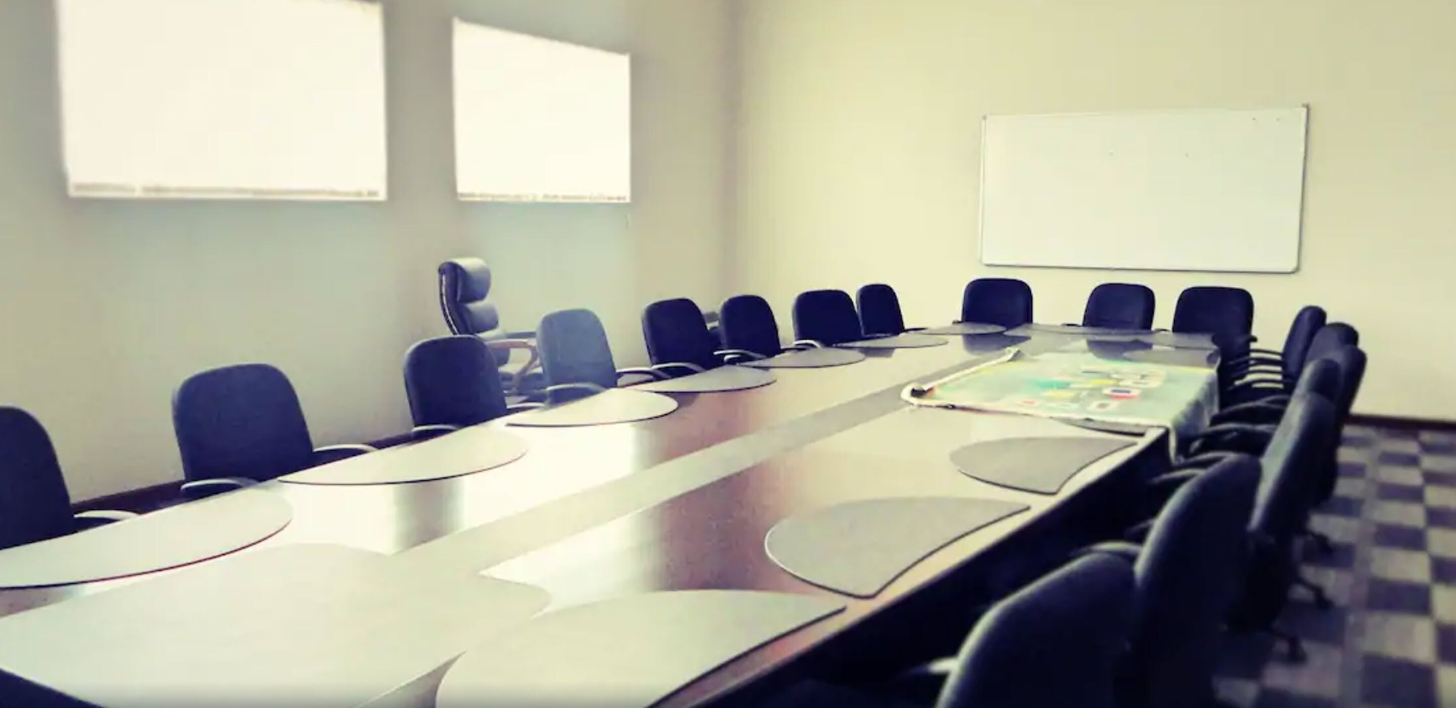 Un salón de conferencias con una larga mesa, varias sillas y una pizarra en la pared.