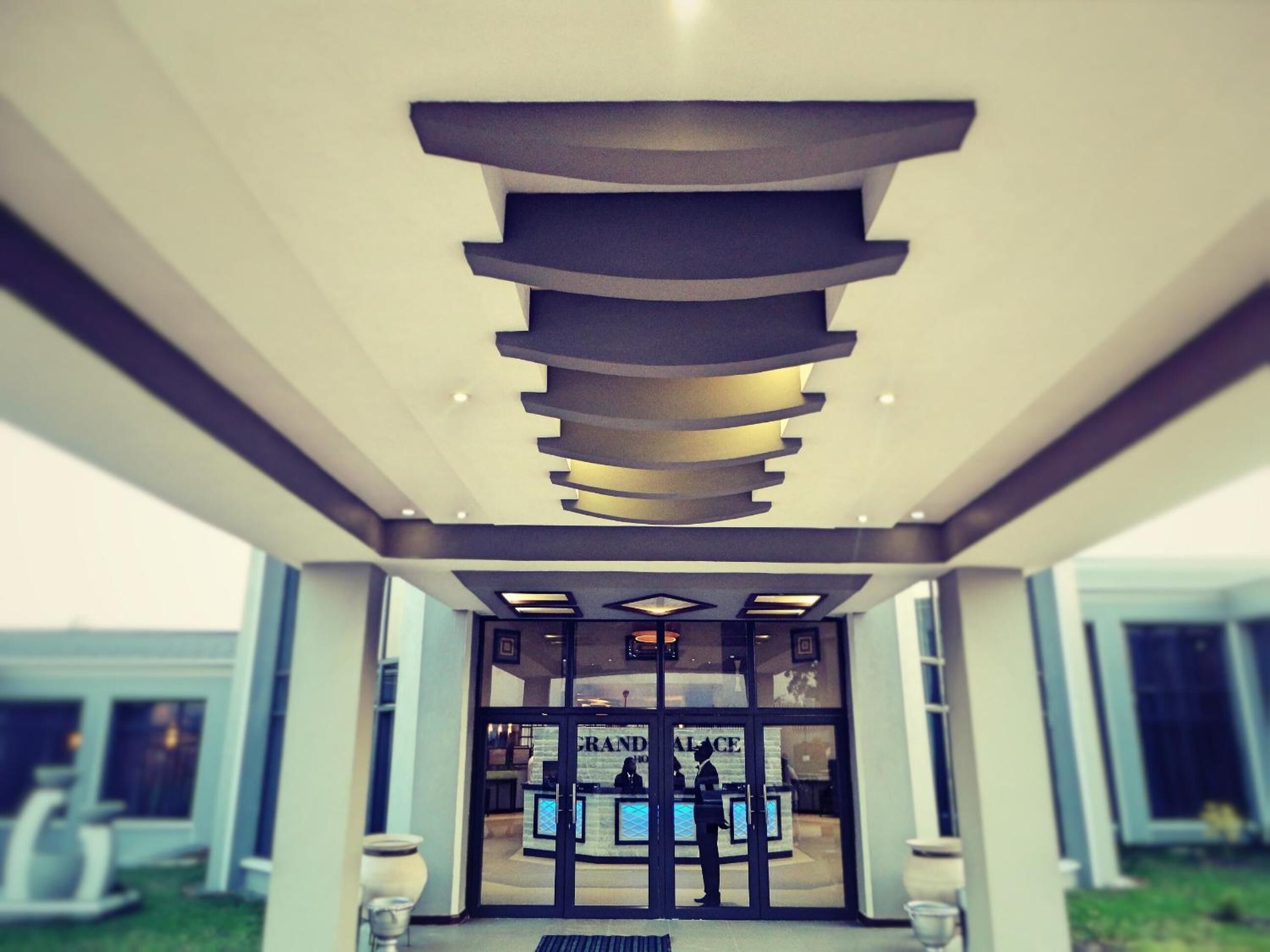 A modern hotel entrance with a unique ceiling design and a reception desk.