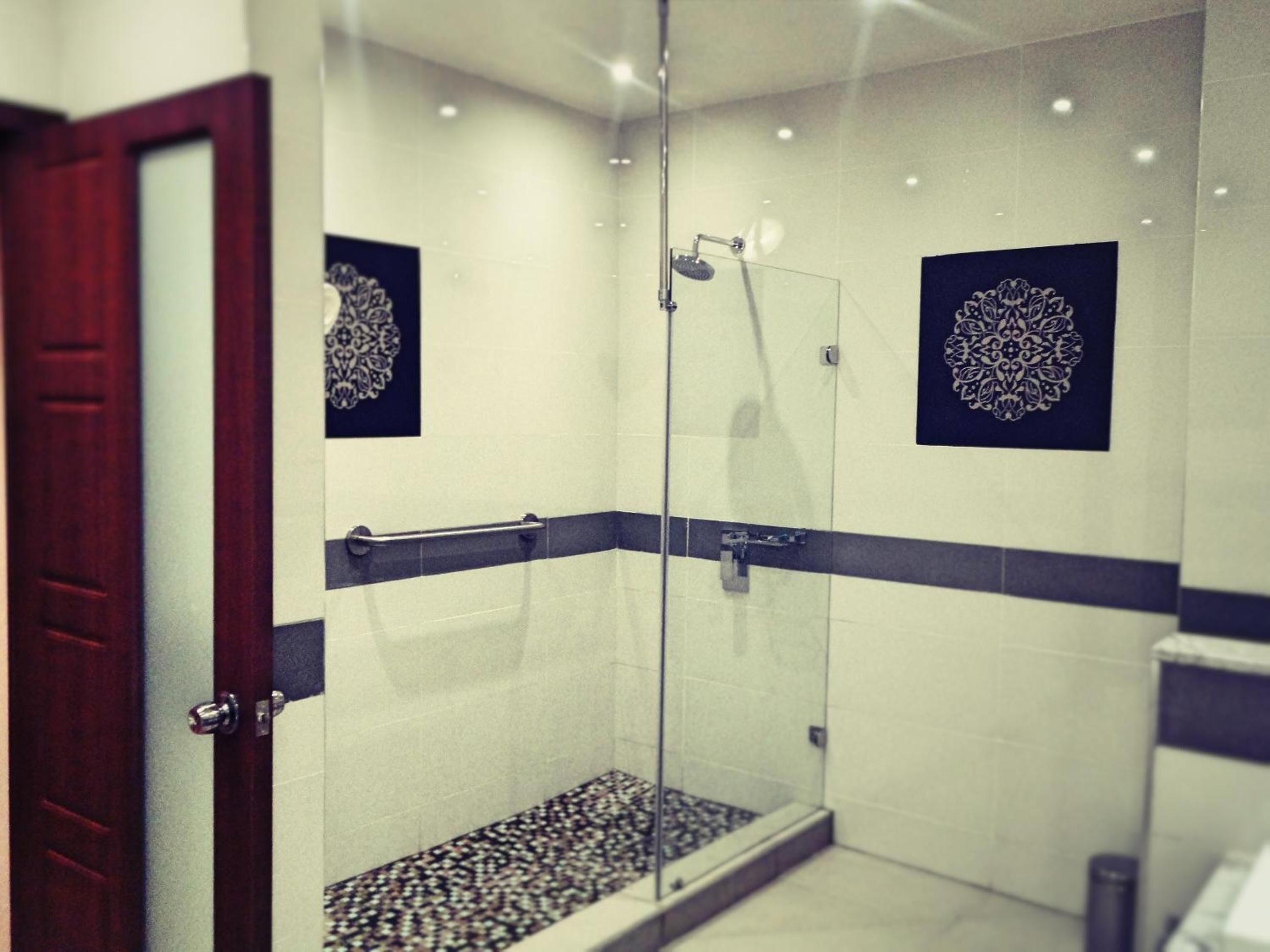 A modern shower with glass doors, a handrail, and decorative wall tiles.