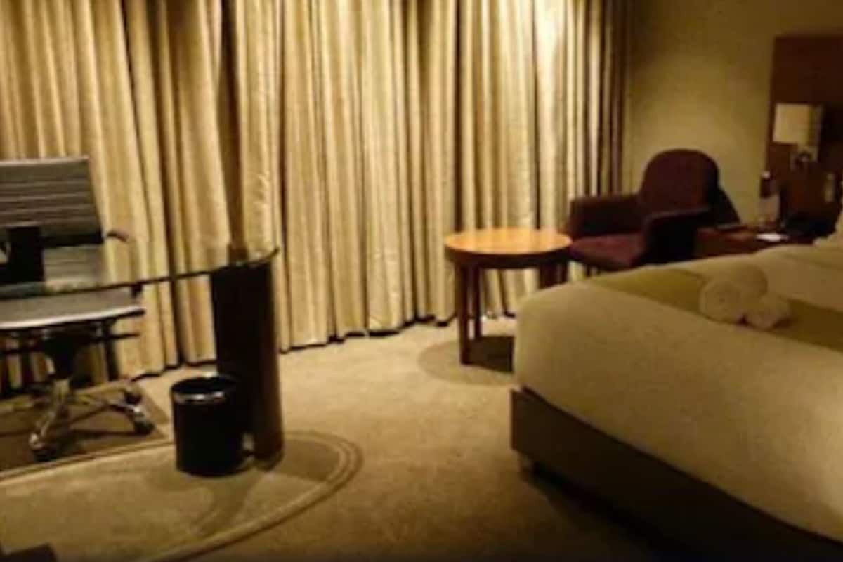 A hotel room with a large bed, a desk with a chair, a small table, and a sofa.
