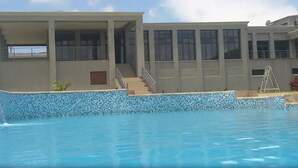 A swimming pool with a tiled edge, a building with a balcony, and a staircase leading to the upper floor. - Grand Palace Hotel (Mzuzu)