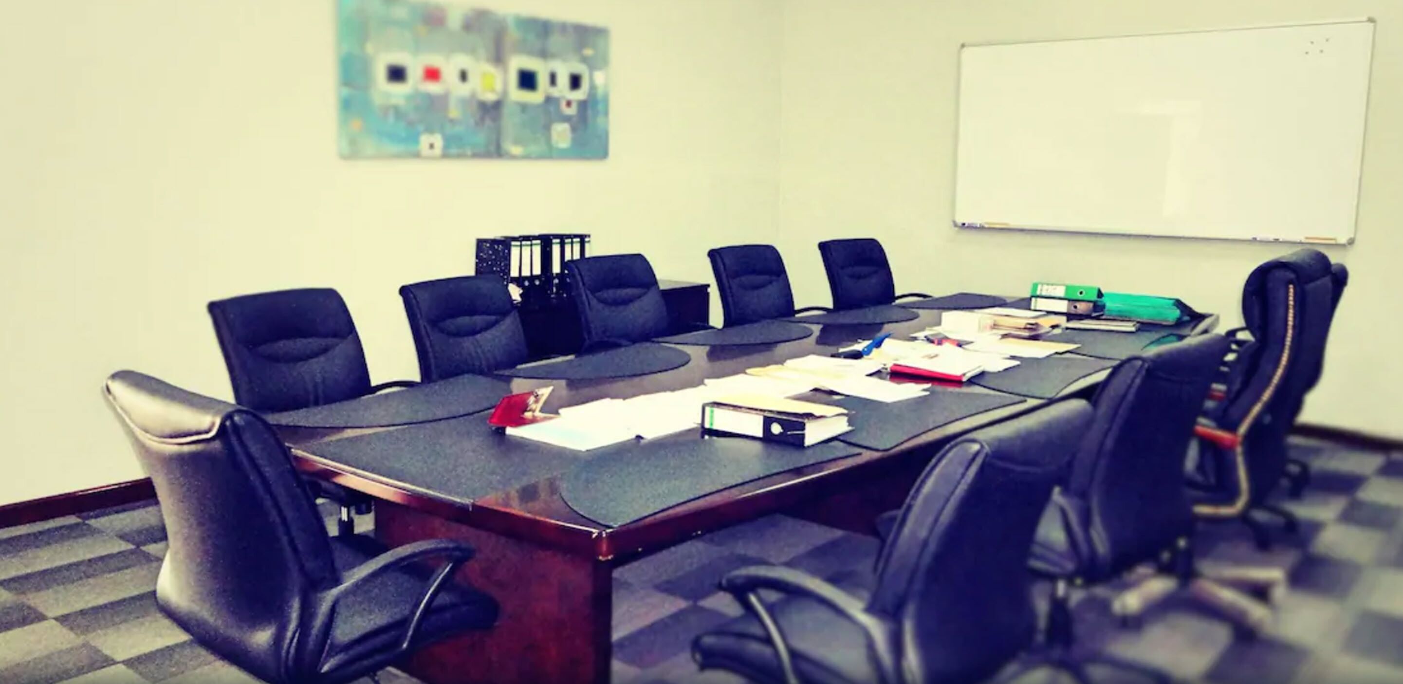 Uma sala de conferências com uma mesa comprida, seis cadeiras pretas e um quadro branco na parede.