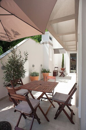 An outdoor patio with a wooden table and chairs, surrounded by potted plants and a large umbrella. - Garni Hotel Arka (Budva)