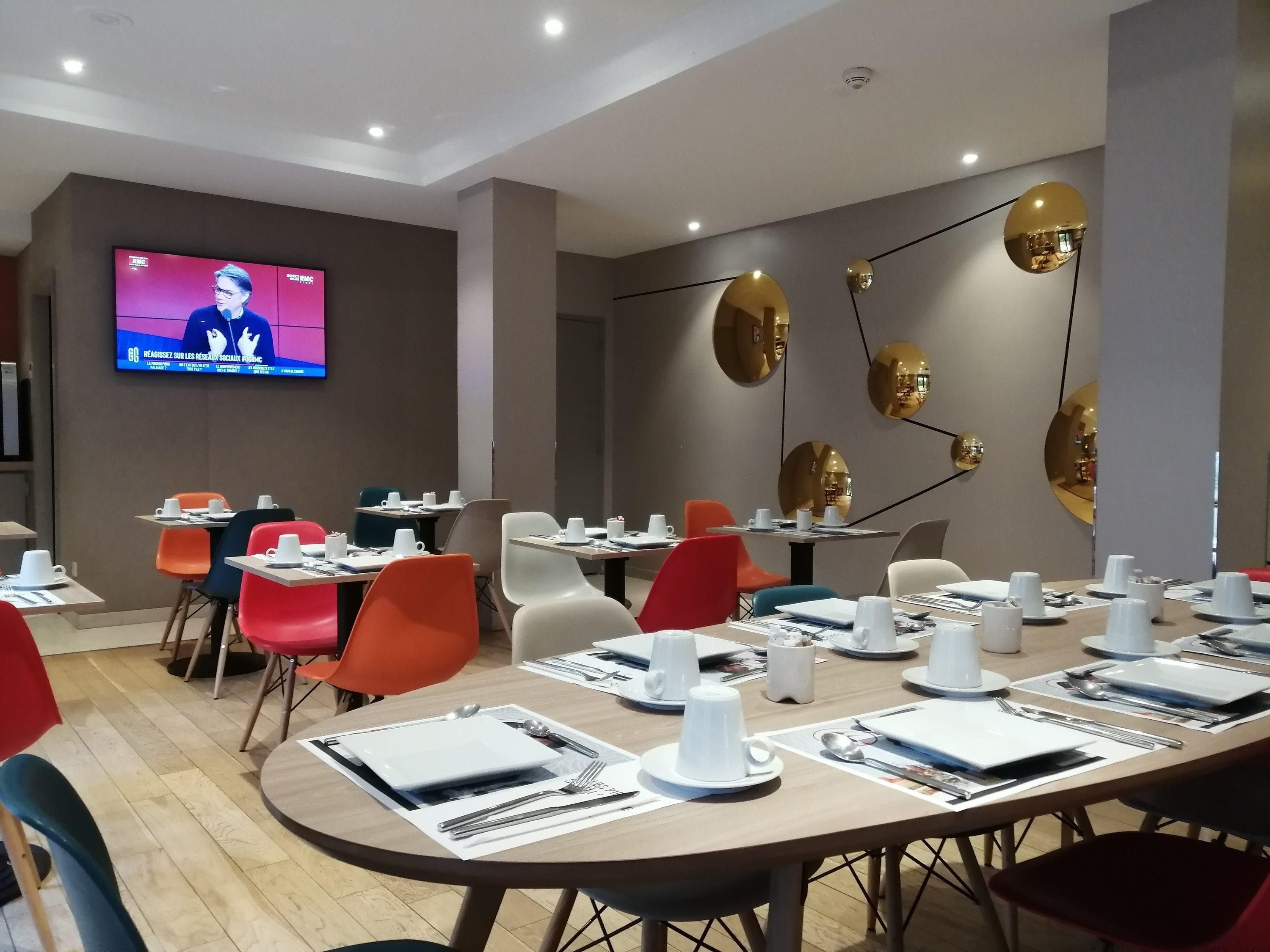 Une salle de conférence avec des tables disposées pour les réunions, un écran de télévision diffusant un programme d’information et des miroirs décoratifs fixés aux murs.
