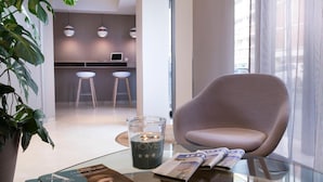 Ein modernes Wohnzimmer mit einem Glastisch, einer Zeitschrift, einer mit „HOME“ beschrifteten Kerze und einer Topfpflanze.