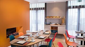 A modern dining area with a long table, colorful chairs, and a kitchen counter with food items.