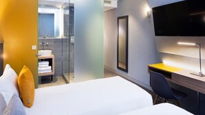 Ein modernes Hotelzimmer mit Bett, Schreibtisch, Stuhl, Fernseher und einer Duschkabine.