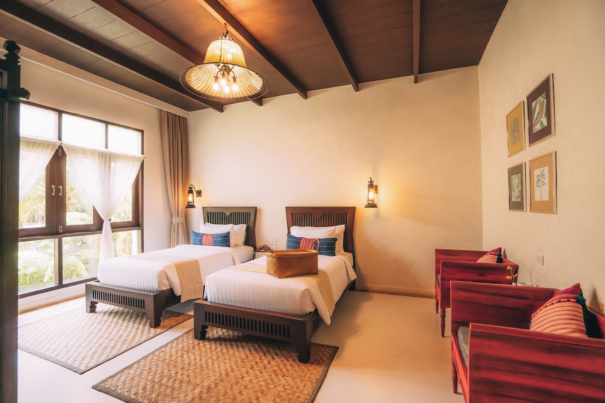 A hotel room with two beds, a sitting area with red sofas, a large window with curtains, and a chandelier.