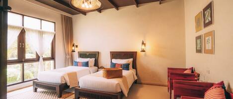 A hotel room with two beds, a sitting area with red sofas, a large window with curtains, and a chandelier.