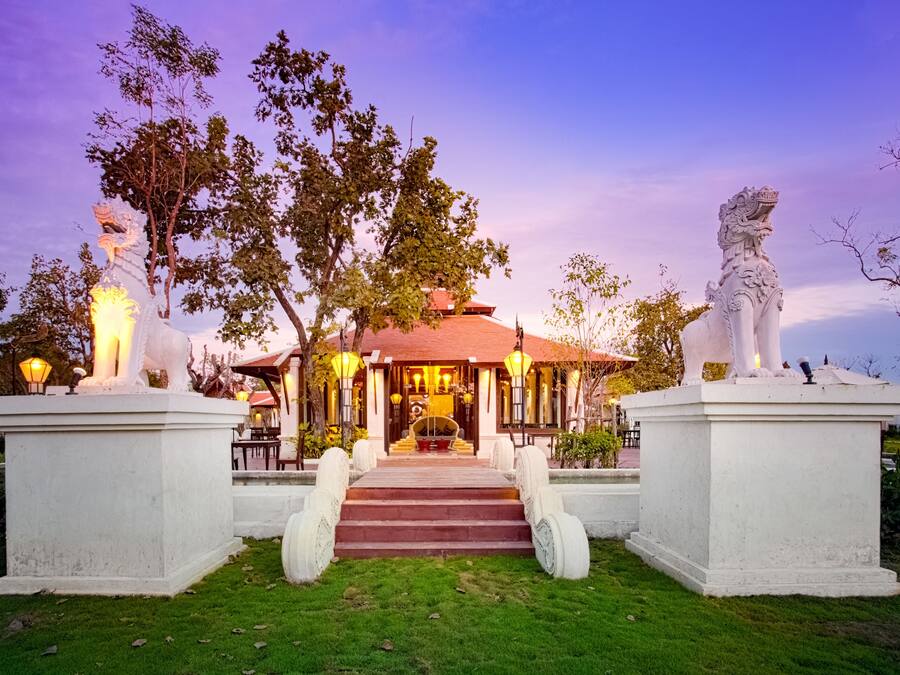Un edificio tradicional con techo rojo, rodeado de estatuas y un jardín bien cuidado.