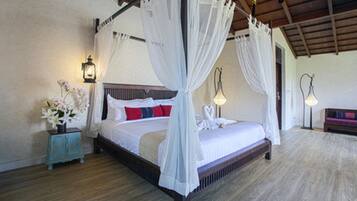 A four-poster bed with white drapes, a wooden headboard, and a bedside table with a vase of flowers.