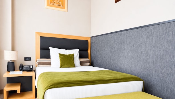 Una habitación de hotel con cama, mesita de noche, lámpara y un pequeño taburete.