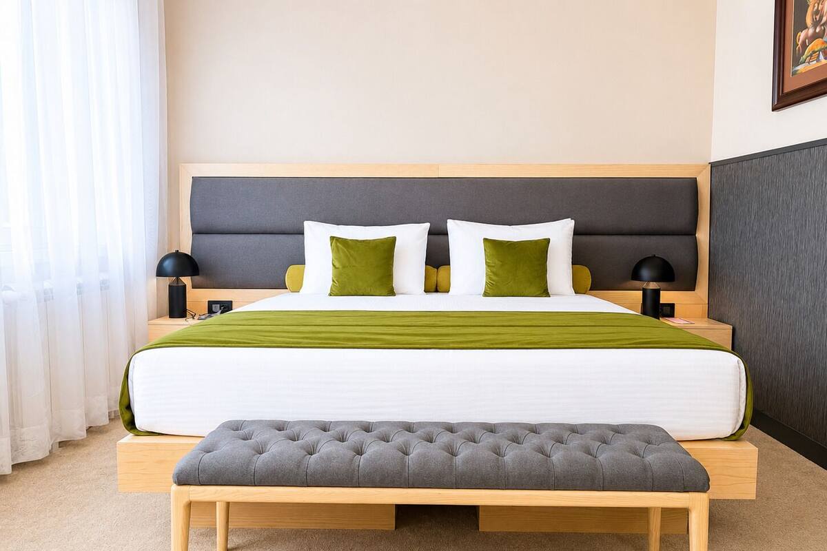 A modern hotel room with a large bed, a bench, and a headboard.