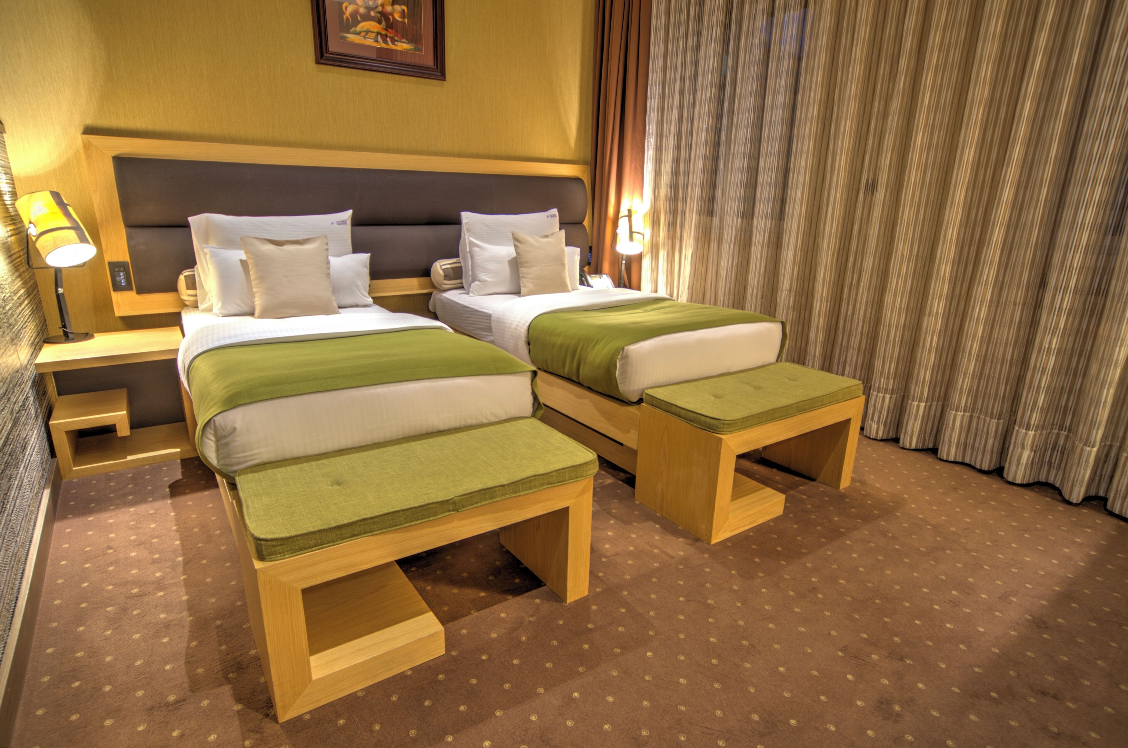 A hotel room with two beds, a nightstand, a lamp, and a curtain.