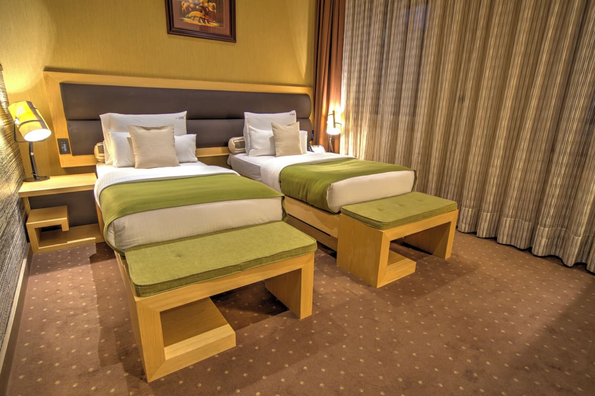 A hotel room with two beds, a nightstand, a lamp, and a curtain.