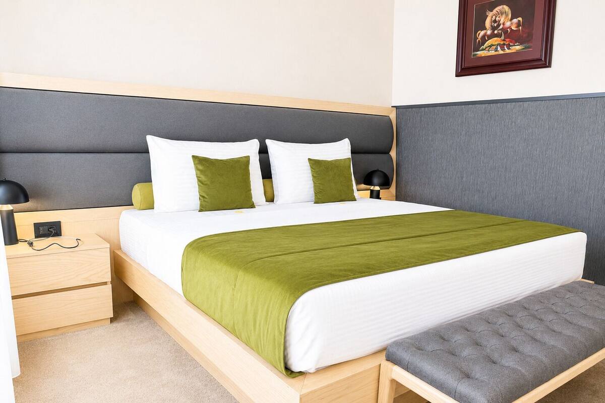 A neatly arranged bedroom with a bed, bedside tables, a bench, and a framed picture on the wall.