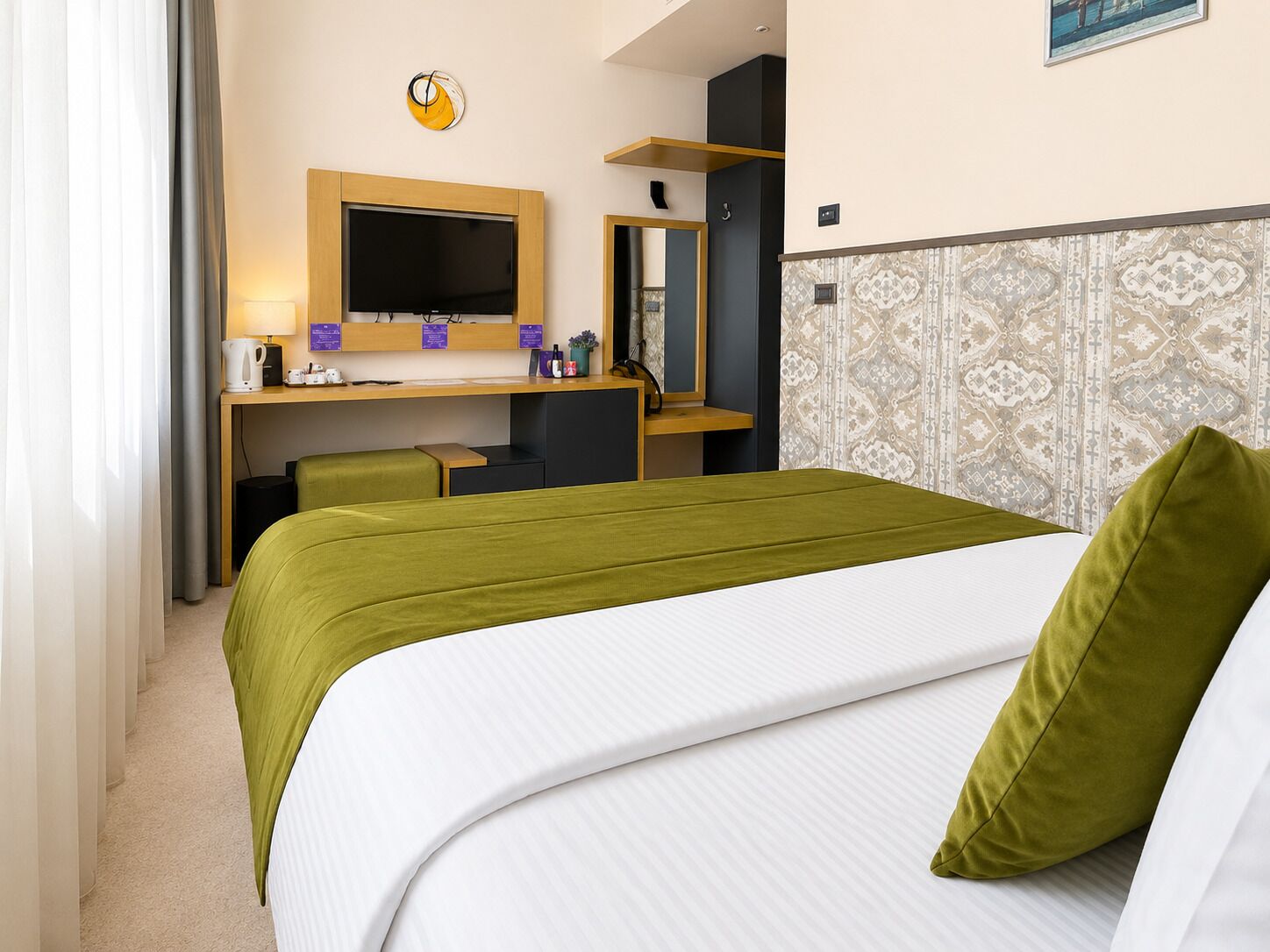 A hotel room with a bed, a desk with a computer, a chair, a television, and a mirror.