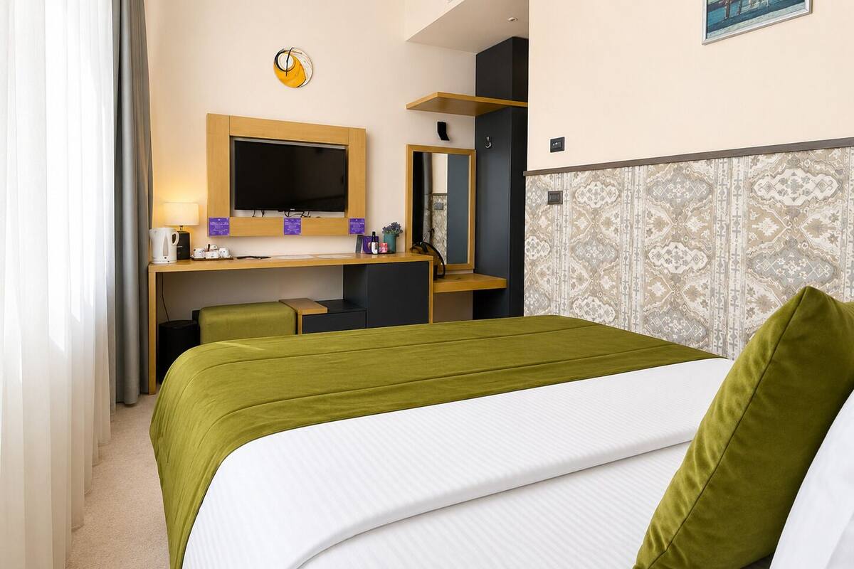 A hotel room with a bed, a desk with a computer, a chair, a television, and a mirror.