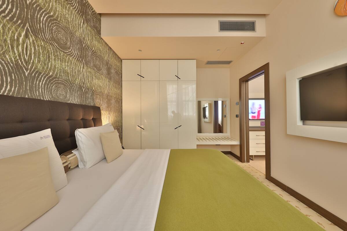 A hotel room with a bed, a TV, a wardrobe, and a mirror.