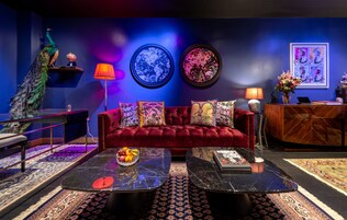Ein luxuriöses Wohnzimmer mit einem üppigen roten Sofa, einer Pfauenstatue und einem Globus auf einem Regal.