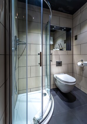 A modern bathroom with a glass-enclosed shower, a white toilet, and a mirror above the sink. - Hux Hotel (London)