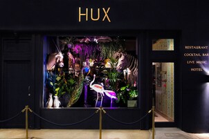 Ein Hotel Eingang mit einem Neonzeichen mit dem Schriftzug 'HUX' und einer Schaufensterpuppe mit verschiedenen Tieren und Pflanzen.