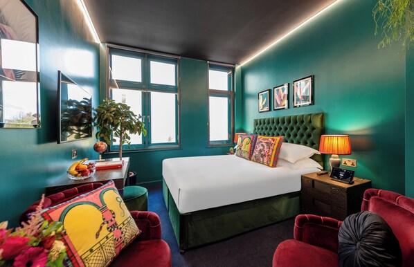 A modern bedroom with a large bed, a desk with a globe, and a red armchair. - Hux Hotel (London)