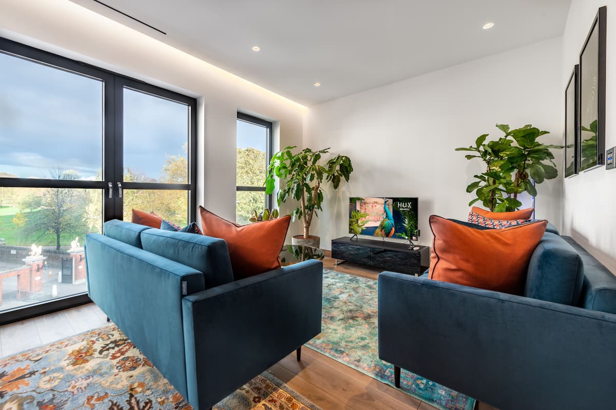 A modern living room with large windows, a blue sofa, a TV, and potted plants.