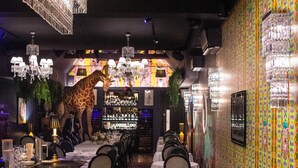 A restaurant with a giraffe statue, chandeliers, and colorful wallpaper.