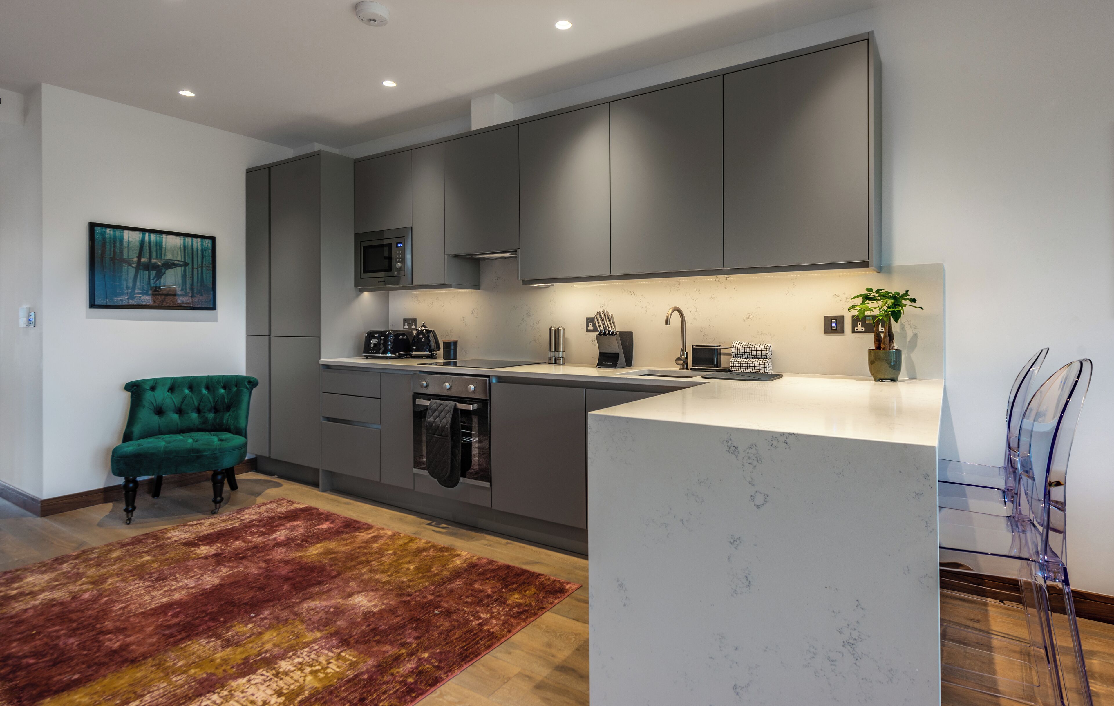 A modern kitchen with grey cabinets, a marble island, and a green armchair.