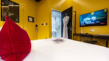 A hotel room with a bed, a red pillow, a TV displaying 'Ozark', and a robe hanging on the door.