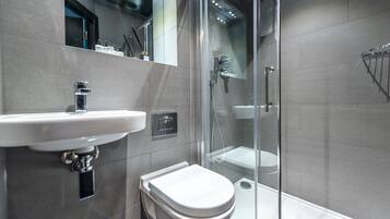 A modern bathroom with a glass-enclosed shower, a white sink, and a toilet.