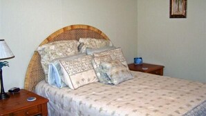 Un dormitorio con cama, mesita de noche, lámpara y un cuadro en la pared.