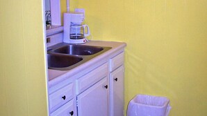Una cocina pequeña con gabinetes blancos, una cafetera y un cubo de basura.