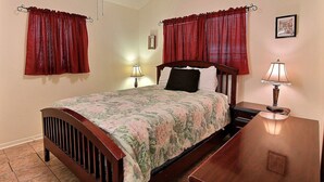 Un dormitorio con cama de madera, colcha estampada, dos lámparas de noche y cortinas rojas.