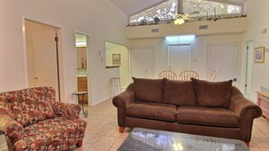 Una sala de estar con un sofá marrón, un sillón estampado y una mesa de centro de vidrio.