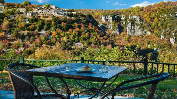 Ein Tisch mit Essen und Gläsern vor einer Berglandschaft mit Gebäuden auf einem Hügel.