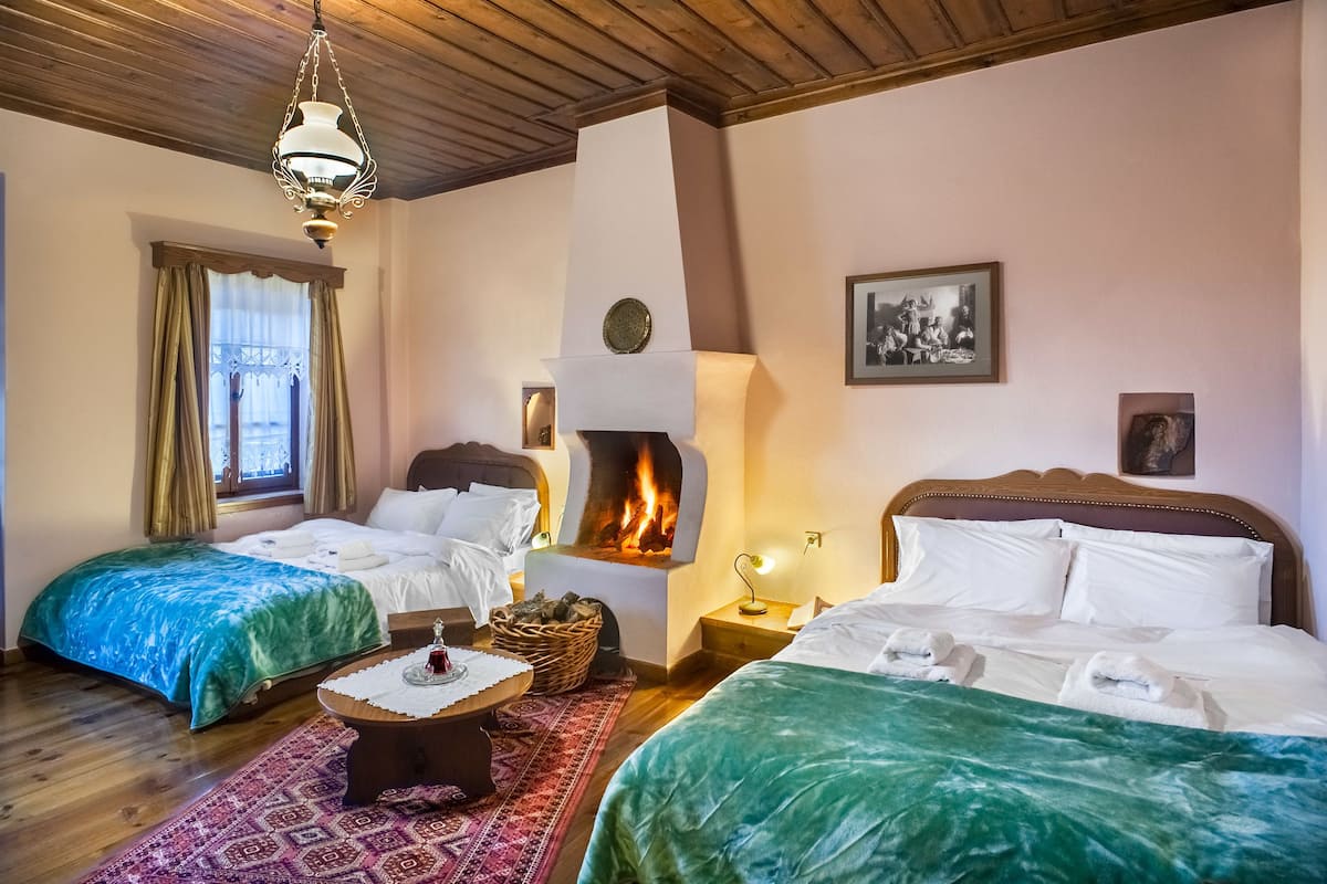 A cozy room with two beds, a fireplace, a wooden ceiling, and a patterned rug.