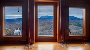Ein Zimmer mit drei großen Fenstern und Blick auf eine gebirgige Landschaft.