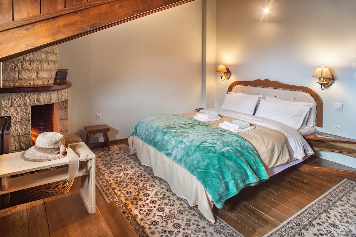 A bedroom with a stone fireplace, a bed with a green blanket, and two wall-mounted lamps.