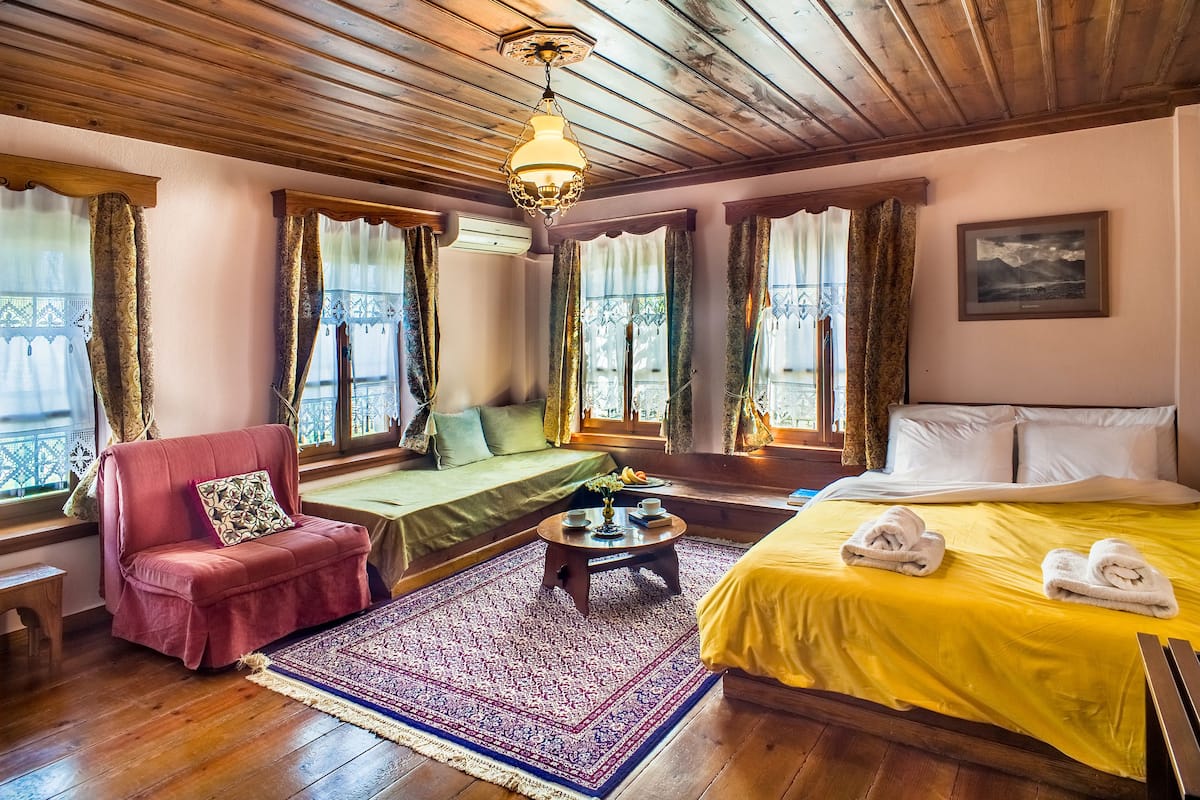 A cozy room with a wooden ceiling, a sofa, a bed with yellow bedding, and a window with curtains.