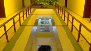A corridor with yellow walls, a central planter with a tree, and a glass table with a plant. - Murat Hotel (Kemer)