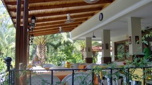 A covered outdoor seating area with tables and chairs, surrounded by greenery and a wooden ceiling. - Murat Hotel (Kemer)