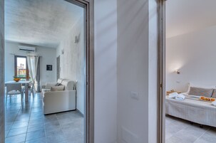 Una habitación de hotel moderna con cama, una mesita con frutero y un área de descanso con sofá y sillones.