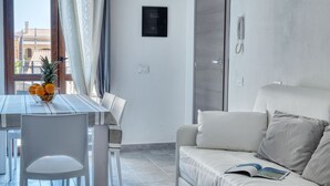 Una sala de estar moderna con un sofá blanco, una mesa de comedor con sillas y una ventana con cortinas.